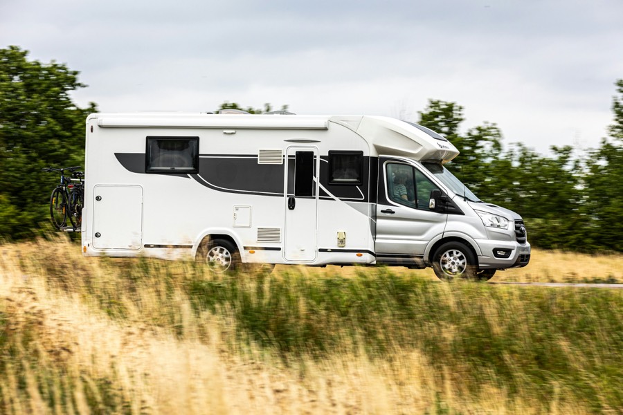 Un camping-car profilé blanc roule au milieu des herbes hautes